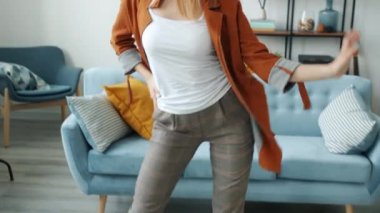 Dans eden ve şarkı söyleyen mutlu genç bir kadın modern kulaklıklarla müzik dinliyor.