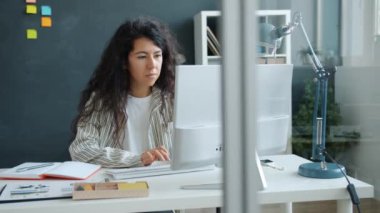 Genç melez bayan bilgisayar yazma ile çalışıyor. Sonra da ofiste not defterine bilgi yazıyor.