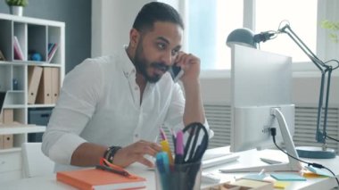 Cep telefonuyla konuşan ve bilgisayarla çalışan genç melez girişimcinin yavaş hareketi