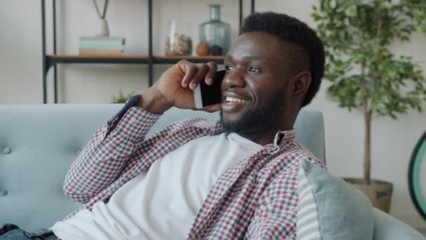 Movimiento lento del hombre afroamericano guapo hablando por teléfono móvil sonriendo en casa — Vídeo de stock