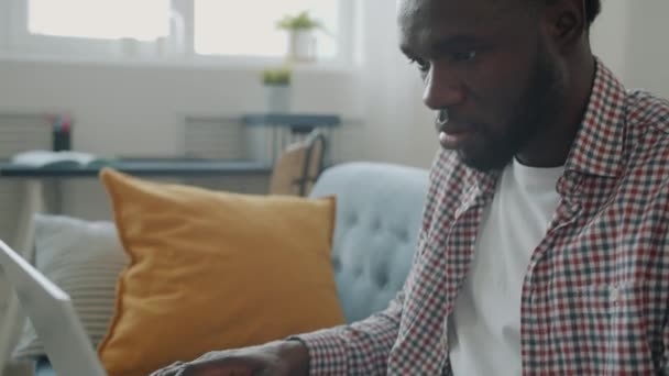 Vážný Afroameričan psaní s notebookem zaneprázdněn prací na volné noze doma
