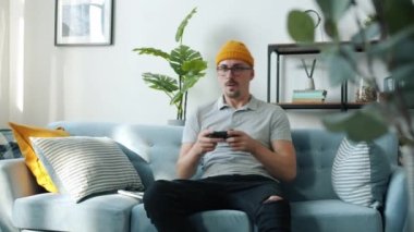 Genç hippi adam elinde joystick ile video oyunu oynuyor. Evde hobi olarak eğleniyor.