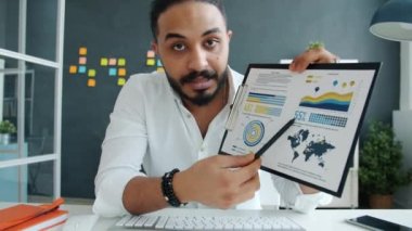 Ofisteki video konferansında konuşan ve grafikleri gösteren melez adamın portresi.