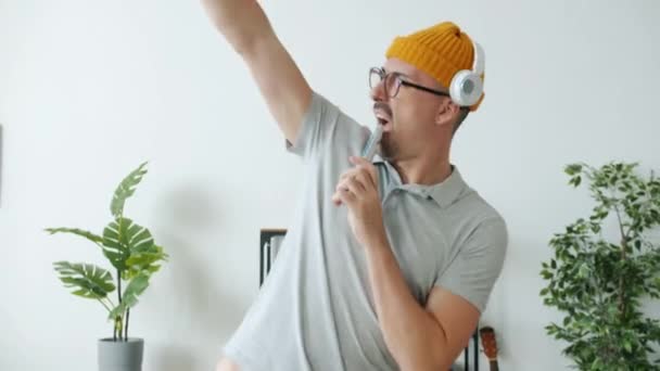 Jeune homme dansant en chantant à distance et écoutant de la musique grâce à des écouteurs à l'intérieur à la maison — Video