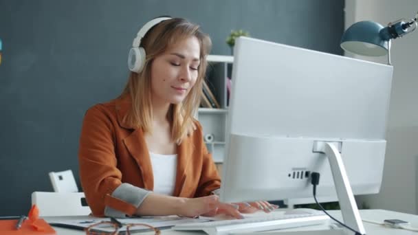 Mouvement lent de la jeune femme d'affaires dansant portant des écouteurs travaillant avec l'ordinateur dans le bureau — Video