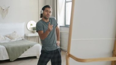 Yatak odasında kulaklık takmış, aynanın önünde dans eden neşeli genç adamın portresi.