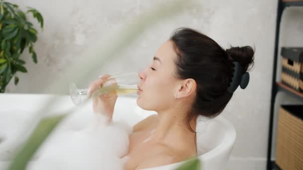 Movimento lento di donna gioiosa bruna che beve dal vetro e si lava nella vasca da bagno a casa — Video Stock