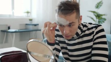 Pandomimci, makyaj malzemesi kullanarak aynaya bakıyor.