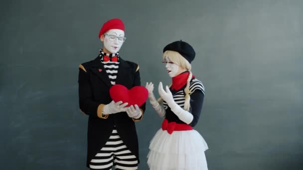 Girl and guy mimes showing heart gestures then kissing on grey background — Stock Video