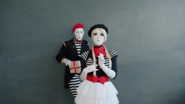 Sevilen adam pandomimci hediye kutusunu gri arka planda sarılan tatlı kıza veriyor.