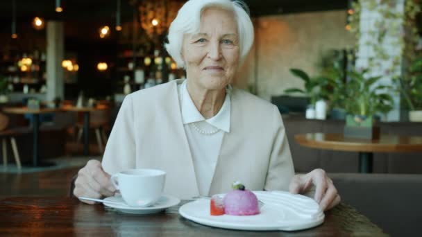 Retrato en cámara lenta de la hermosa señora mayor sentada en la mesa en la cafetería con comida y bebida — Vídeos de Stock