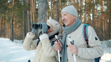 Üst düzey kadın dürbünle doğayı keşfediyor ve yaşlı bir adamla sohbet ediyor.