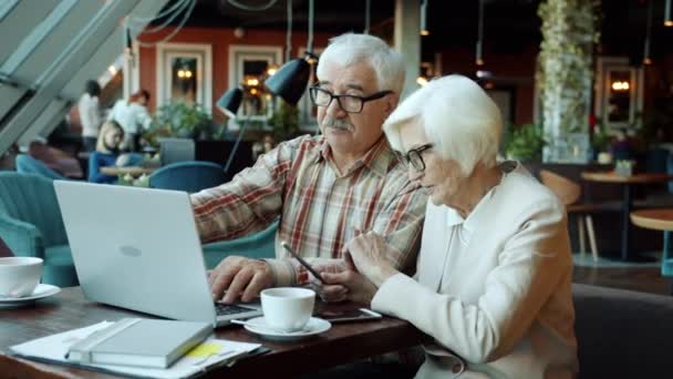 Personas mayores socios de negocios discutiendo finanzas y sonriendo mirando a la pantalla del ordenador portátil en la mesa en la cafetería — Vídeo de stock