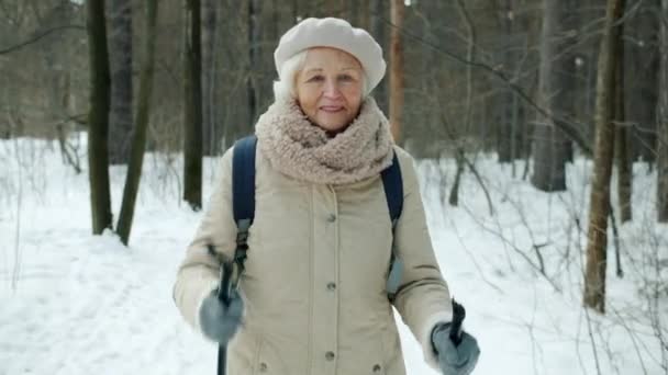 Dolly shot van mooie senior sportvrouw genieten van nordic walking in winterpark — Stockvideo