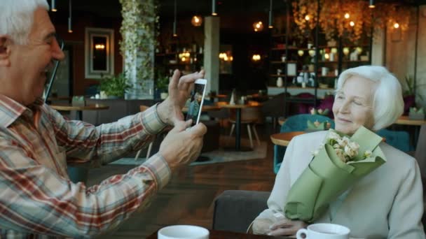 İhtiyar, kafede akıllı telefon kamerasıyla yaşlı bir kadının fotoğraflarını çekiyor. — Stok video