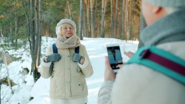 Feliz señora de edad avanzada posando para la cámara del teléfono inteligente en el parque nevado en invierno — Vídeo de stock