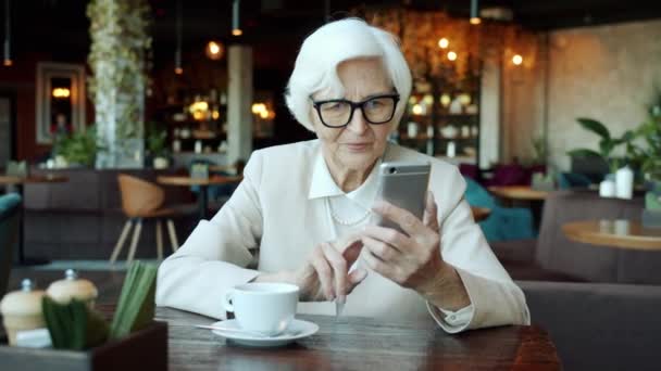 Fröhliche Seniorin bedient Smartphone-Touchscreen und lächelt im Café — Stockvideo