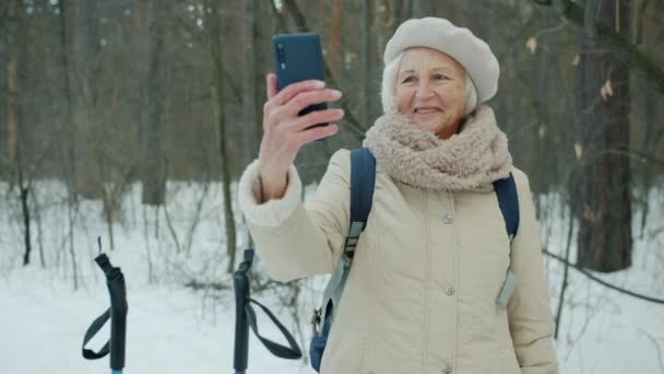 Hermosa señora mayor tomando selfie en el parque de invierno utilizando la cámara del teléfono inteligente pose sonriente — Vídeos de Stock