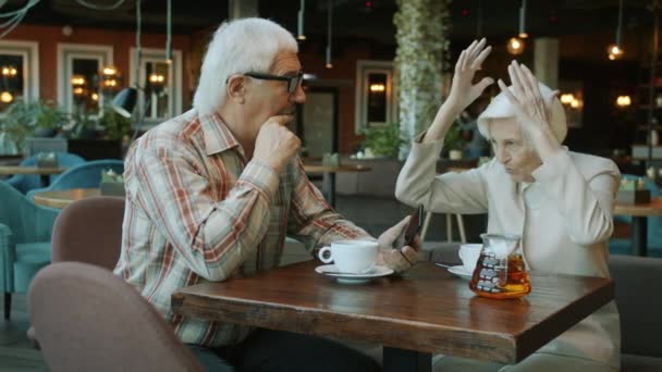 Медленное движение красивой пожилой пары, говорящей и жестикулирующей за столом в кафе — стоковое видео