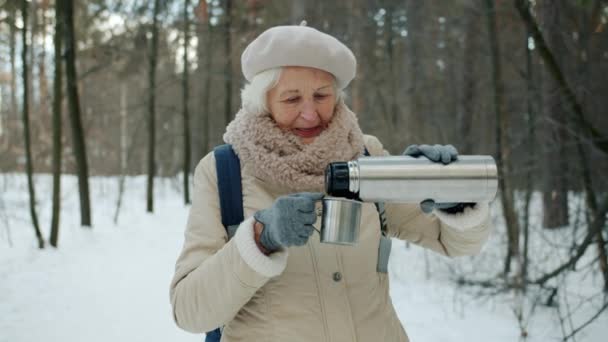 Медленное движение пожилой туристки, наливающей горячий чай из термоса в лесу зимой — стоковое видео