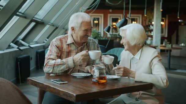 Emeryci mężczyzna i kobieta brzęczą filiżanki herbaty i piją ciesząc się czasem w kawiarni — Wideo stockowe