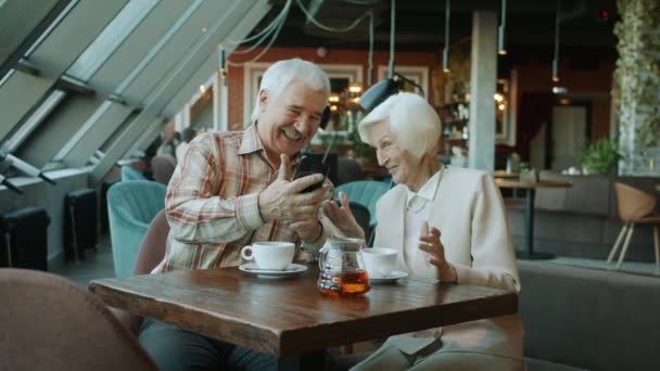 Homme et femme âgés regardant l'écran du smartphone et discutant du contenu riant dans le café — Video