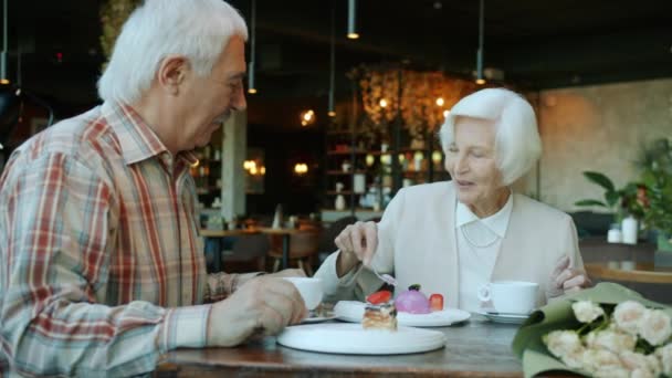 Веселая пожилая женщина угощает мужа вкусным тортом, разговаривая смеясь в кафе — стоковое видео