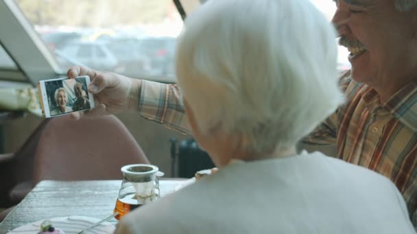 Vissza kilátás boldog család idősebb férfi és nő, hogy szelfi nézi okostelefon képernyő kávézóban — Stock videók