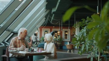 Yaşlı bir adam yaşlı bir kadınla sohbet ediyor. Bardağına çay dolduruyor. Karısına restoranda bakıyor.