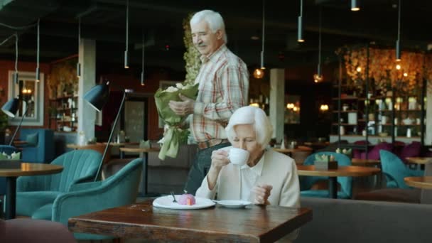 Zeitlupe einer Seniorin beim Mittagessen im Café, während der Mann ihr Blumen bringt — Stockvideo