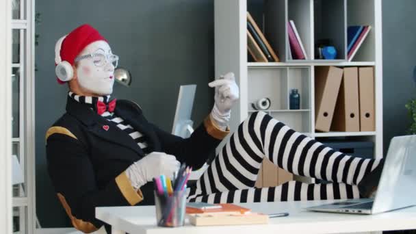 Funny guy mime listening to music through headphones and playing invisible guitar in office — Stock Video
