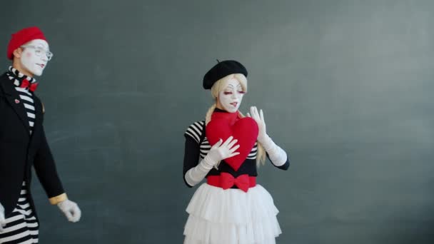 Man and woman mimes holding big red heart and kissing on grey background — Stock Video