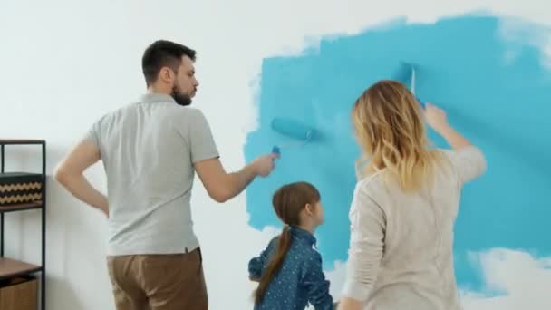 Back view of adorable young family mum dad and daughter painting wall in apartment — Stock Footage Back view of adorable young family mum dad and daughter painting wall in apartment Stock Footage