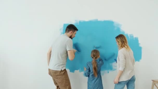 Joyful familie met kind verbouwen huis schilderen muur en dansen genieten van muziek samen — Stockvideo