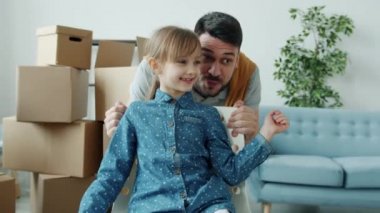 Küçük bir kızı sandalyeye oturtup yeni daireyi gösteren kızıyla konuşan genç adamın Dolly 'nin fotoğrafı.