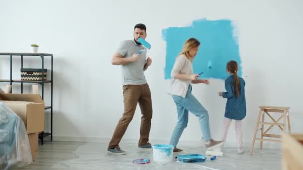 Glückliche junge Leute Eltern und Tochter tanzen und singen Malwand im Haus mit Umbau beschäftigt — Stockvideo