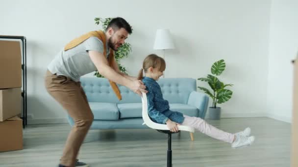 Φροντίζοντας τον μπαμπά διασκεδάζοντας με την κόρη σπρώχνοντας καρέκλα με το παιδί γαργαλώντας γέλιο στο νέο σπίτι — Αρχείο Βίντεο