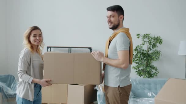 Retrato de casal feliz sorrindo olhando para câmera segurando caixa de papelão durante a mudança para a nova casa — Vídeo de Stock