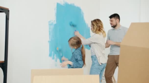 Klein meisje schilderij muur met ouders dansen en plezier hebben genieten van muziek binnen thuis — Stockvideo
