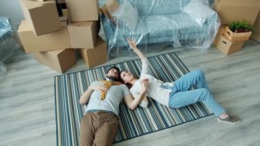 Yeni evin zemininde konuşan ve el kol hareketi yapan neşeli çiftin yüksek açılı görüntüsü.