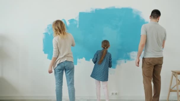 Vista posterior de la joven familia madre padre y niño pared de pintura en el interior de la habitación de renovación de casa — Vídeos de Stock