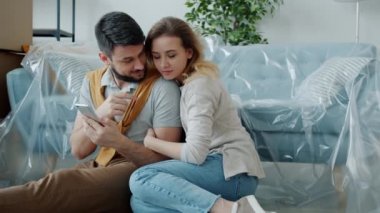 Akıllı telefon kullanan genç bir adam ve kadının yeni bir dairede birlikte oturması.