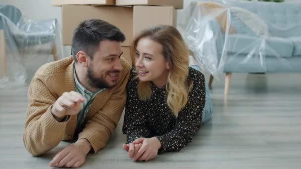 Boldog srác kulcsot ad a csinos barátnőjének, aztán csókolózik a padlón egy új lakásban, beszél. — Stock videók