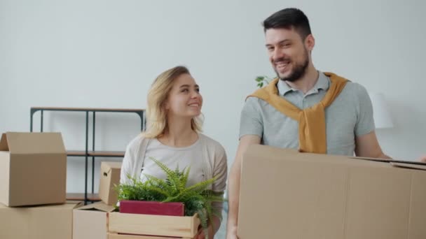 Slow motion portrait of girl and guy holding boxes smiling looking at camera in new apartment — Stock Video