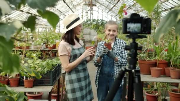 Jonge vrouw en kind boeren opnemen video praten tonen duimen-up in de kas met behulp van camera — Stockvideo