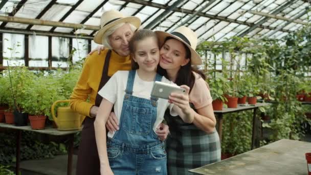 Chica tomando selfie con la madre y la abuela en el hermoso invernadero verde con el teléfono inteligente — Vídeo de stock