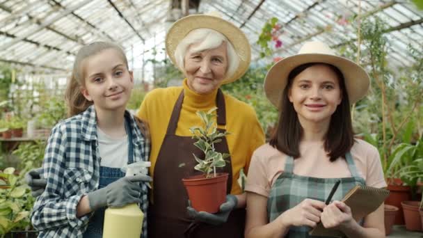 Movimento lento da avó mãe família e criança em estufa segurando garrafa de spray de plantas e notebook — Vídeo de Stock