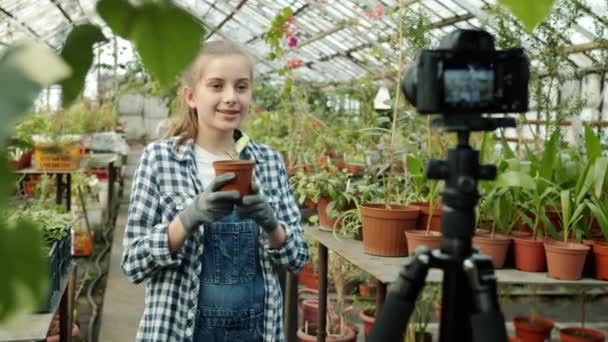 Câmera lenta de menina bonito vlogger segurando planta gravação de vídeo em estufa mostrando como gesto — Vídeo de Stock
