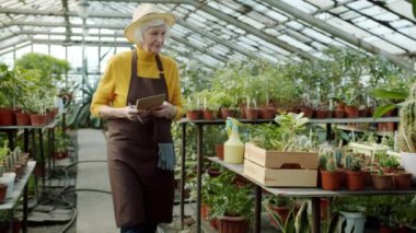 Yaşlı çiftçi serada yürüyor bitkileri kontrol ediyor deftere envanter bilgileri yazıyor