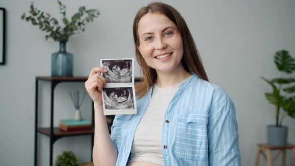 Porträt einer schönen schwangeren Frau, die mit einem Ultraschallbild lächelt und in die Kamera blickt — Stockvideo